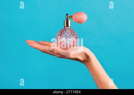 Anonyme schlanke junge weibliche Hand hält auf Palme Vintage Kristallschliff klassisches Parfüm in transparenter Flasche mit Gasbeutel Zerstäuber Spray montiert oben Stockfoto