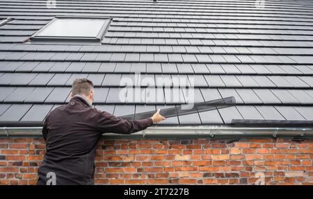 Der Mensch legt ein Rinnengittergewebe an die Regenrinne, um die Rinne vor Blättern zu schützen. Stockfoto