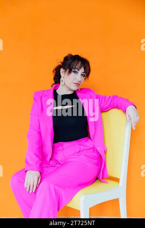 Eine Frau in hellen Kleidern sitzt auf einem Stuhl auf einem orangefarbenen Hintergrund Stockfoto