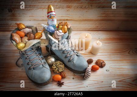 Stiefel gefüllt mit Süßigkeiten, Schokolade Santa und Weihnachtsdekoration auf hölzernem Hintergrund mit Kerzen, Tradition auf dem deutschen Nikolaus Tag, was Nicho bedeutet Stockfoto