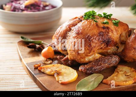 Festliches gebratenes Huhn frisch aus dem Ofen mit Äpfeln, Kumquat, Gewürzen und Kräutern serviert mit Rotkohl auf einem Holztisch, Geflügelessen zu Weihnachten Stockfoto