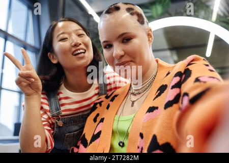 POV einer lächelnden jungen Frau mit kreativem Haar, die Selfie im Schönheitssalon mit Friseurin macht Stockfoto