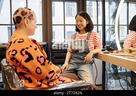 Porträt einer lächelnden asiatischen Frau als Friseurin, die im Salon mit kreativem Haar spricht Stockfoto