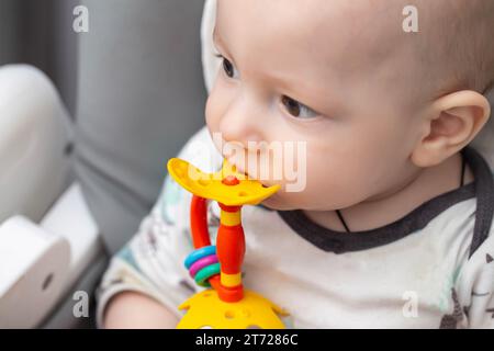 Porträt eines Kindes, das ein mehrfarbiges Spielzeugmassagegerät zum Zahnen bei Kindern beißt. Hilfe beim Zahnen. Zahnfleischjucken und Speichelfluss, Zahnzugang Stockfoto