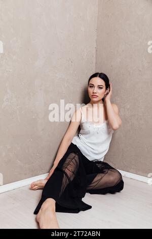 Eine brütende Frau in schwarzer Hose sitzt in einer Ecke Stockfoto