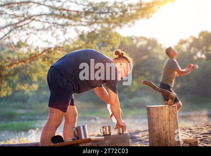 Ein brutaler Mann mit Bart bereitet Tee in Tassen auf einem Campingplatz in der Natur zu. Stockfoto