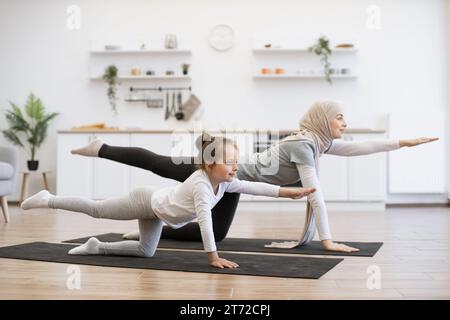 Schöne Mutter mit ihrem Mädchen, die zusammen Yoga-Übungen in der Küche praktiziert. Stockfoto