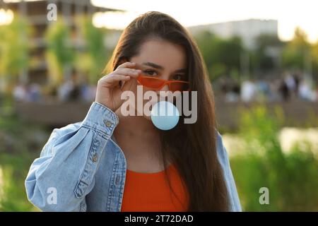 Schöne junge Frau mit Sonnenbrille, die Kaugummi im Freien bläst Stockfoto