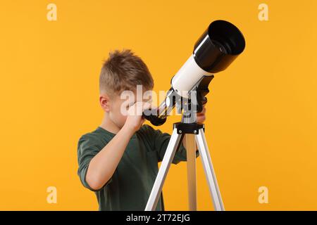 Kleiner Junge, der Sterne durch ein Teleskop auf orangefarbenem Hintergrund ansieht Stockfoto