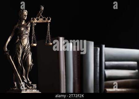 Statue von Lady Justice in der Nähe von Büchern auf schwarzem Hintergrund, Platz für Text. Symbol für eine gerechte Behandlung nach dem Gesetz Stockfoto