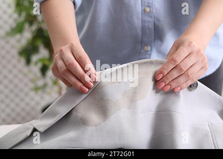 Frau zeigt Flecken vom Kaffee auf der Jacke vor verschwommenem Hintergrund, Nahaufnahme Stockfoto