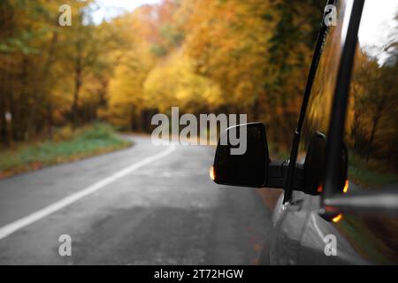 Modernes Auto auf Asphaltstraße in der Nähe des Herbstwaldes, Nahaufnahme. Leerzeichen für Text Stockfoto