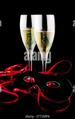 Zwei Flöten mit Champagner in der Nähe einer Karnevalsmaske auf schwarzem Hintergrund Stockfoto