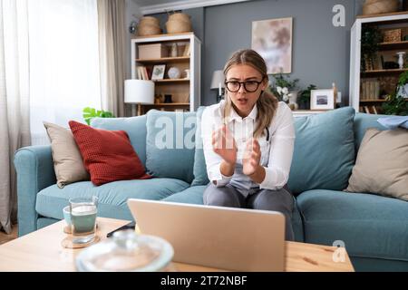 Junge Ärztin, die von zu Hause aus arbeitet, sitzt auf Sofa und hat Videoanruf mit nervösen kranken Patienten, die Menschen hören und sich um sie kümmern. Prof Stockfoto