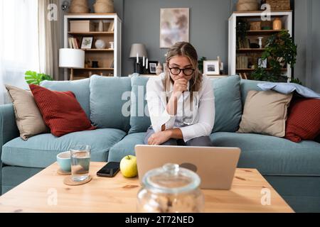 Junge Ärztin, die von zu Hause aus arbeitet, sitzt auf Sofa und hat Videoanruf mit nervösen kranken Patienten, die Menschen hören und sich um sie kümmern. Prof Stockfoto