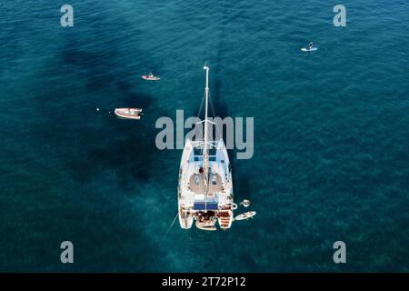 Drohnenblick auf den Katamaran im blauen Meer mit schwimmenden Personen im Sommer. Reisehintergrund. Kreuzfahrturlaub. Stockfoto