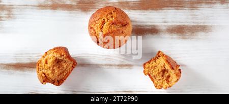 Gebrochene orangene Muffins auf einem rustikalen Küchentisch Panorama, einfaches Backen, flache Lay-Shot über dem Kopf mit Kopierraum Stockfoto