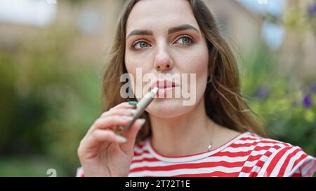 Junge blonde Frau, die Vaper im Park raucht Stockfoto