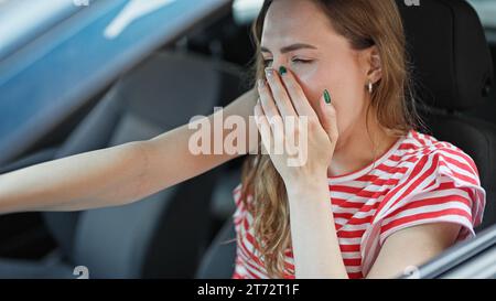 Junge blonde Frau müde, Auto zu fahren und auf der Straße zu gähnen Stockfoto