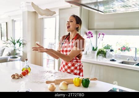 Junge schöne hispanische Frau lächelt zuversichtlich Teig Pizza mit den Händen in der Küche halten Stockfoto