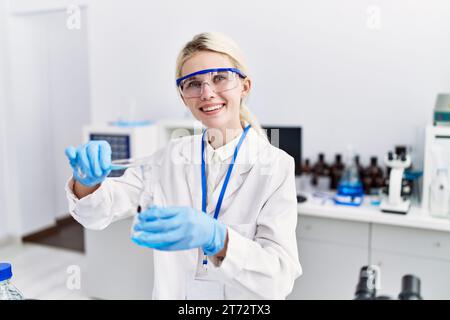 Junge blonde Wissenschaftlerin, die im Labor Flüssigkeit auf das Reagenzglas gießt Stockfoto