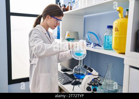 Junge blonde Wissenschaftlerin, die im Labor Flüssigkeit auf das Reagenzglas gießt Stockfoto