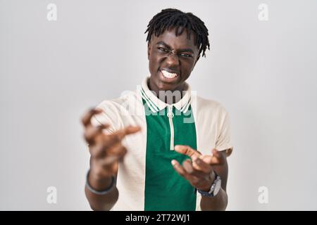 Afrikanischer Mann mit Dreadlocks, der über isoliertem Hintergrund steht und frustriert vor Wut brüllt, Hände versuchen zu erwürgen, schreien verrückt Stockfoto