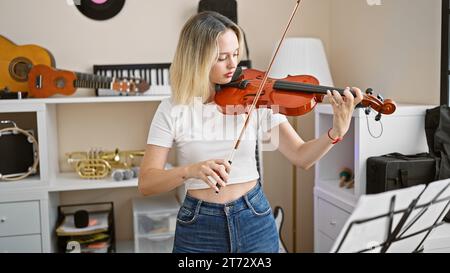 Junge blonde Musikerin, die im Musikstudio Violine spielt Stockfoto