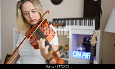 Junge blonde Musikerin, die im Musikstudio Violine spielt Stockfoto