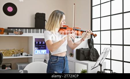 Junge blonde Musikerin, die im Musikstudio Violine spielt Stockfoto