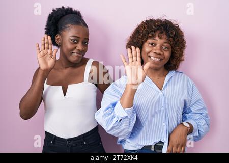 Zwei afrikanische Frauen, die über rosa Hintergrund stehen und nicht Hallo sagen, glücklich und lächelnd, freundliche Willkommensgeste Stockfoto