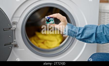 Junge Rothaarige, die Kleidung wäscht und Waschmittelbeutel auf Waschmaschine im Waschraum legt Stockfoto