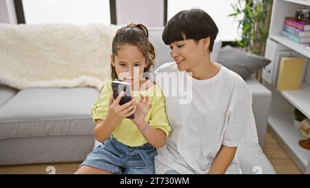 Glückliche Mutter und Tochter sitzen zuhause auf einem bequemen Sofa, lachen und genießen lustige Smartphone-Nachrichten, die positive Freude zwischen Casua ausstrahlen Stockfoto