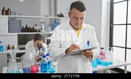 Wissenschaftler arbeiten im Labor zusammen, konzentrieren sich ernsthaft auf ihre Forschung, schreiben auf Zwischenablage, verwenden Mikroskop Stockfoto