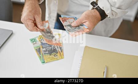 Gutaussehender kaukasischer Geschäftsmann mittleren Alters, der Stapel australischer Dollar im Amt zählt und Investitionserfolg in Schwung nimmt Stockfoto