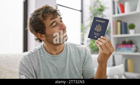 Ein glücklicher junger Mann, der zu Hause auf seinem Sofa sitzt, grinst von Ohr zu Ohr und stellt seinen Pass der vereinigten staaten zur Schau. Dieses selbstbewusste, bärtige, blonde Erwachsene ich Stockfoto
