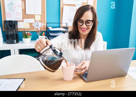 Junge schöne hispanische Geschäftsarbeiterin, die im Büro Kaffee auf die Tasse gießt Stockfoto