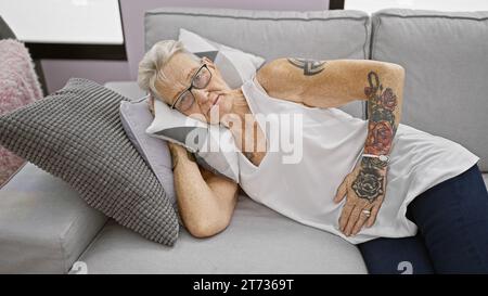 Unglückliche grauhaarige ältere Frau, die unter starken Magenschmerzen leidet, während sie sich zu Hause auf dem Sofa ausruht Stockfoto