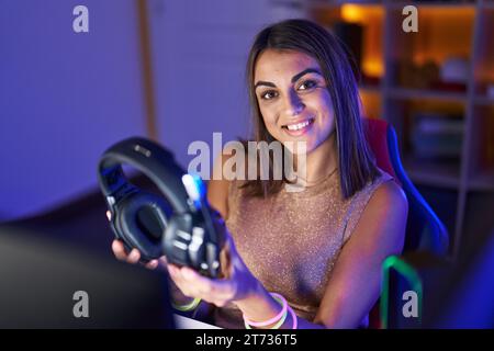 Junge schöne hispanische Frau streamer lächelnd zuversichtlich hält Kopfhörer im Spielsalon Stockfoto