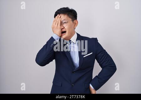 Junger asiatischer Mann mit Business-Anzug und Krawatte, der müde gähnt und Gesicht, Auge und Mund mit der Hand bedeckt. Das Gesicht schmerzt bei Schmerzen. Stockfoto