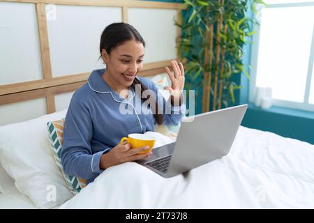 Eine junge arabische Frau trinkt Kaffee und hat Videoanrufe im Schlafzimmer Stockfoto