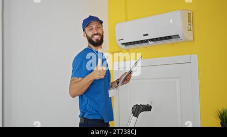 Junger hispanischer Techniker, der die Klimaanlage repariert, indem er zu Hause die Daumen nach oben drückt Stockfoto