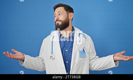 Junger hispanischer Arzt, ahnungslos über isolierten blauen Hintergrund Stockfoto