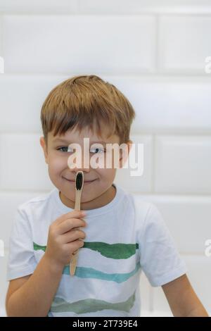 Niedlicher 5-jähriger Junge, der im Badezimmer Zähne mit einer Bambuszahnbürste mit schwarzen Borsten putzt. Stockfoto