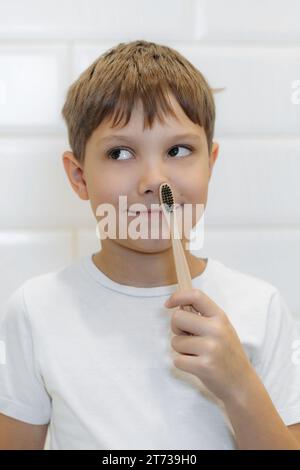 Netter 8-jähriger Junge, der im Badezimmer Zähne mit Bambuszahnbürste mit schwarzen Borsten putzt. Stockfoto