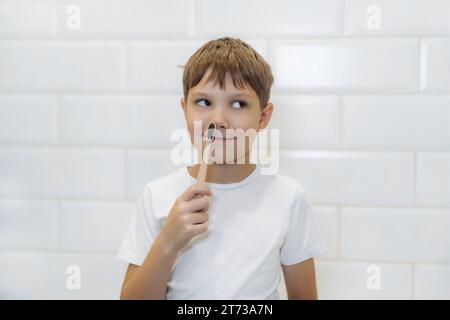 Netter 8-jähriger Junge, der im Badezimmer Zähne mit Bambuszahnbürste mit schwarzen Borsten putzt. Stockfoto