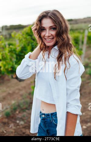 Eine Frau in einem weißen Hemd in einem Weinberg mit grünen Blättern Stockfoto