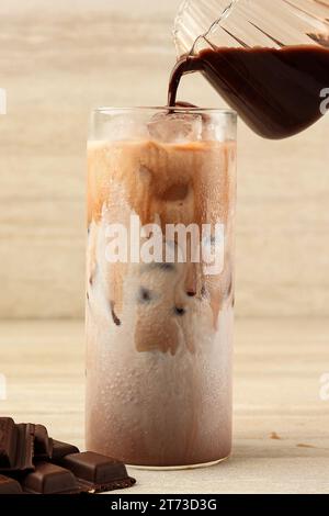 Gießen Sie Schokoladensauce in ein großes Glas mit frischer Milch und Eis. Kaltes Getränk Sommerkonzept Stockfoto