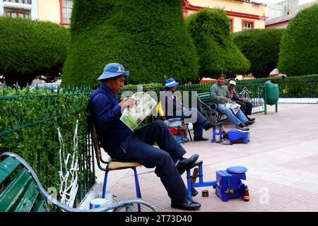 Ein Schuhputzer liest eine Zeitung, während er auf den Plaza de Armas in Puno, Peru, wartet Stockfoto