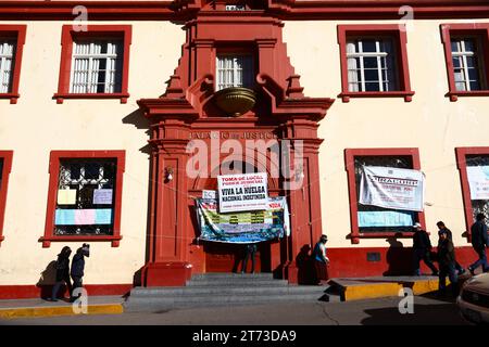 Die Menschen gehen an Schildern am Eingang des Palacio de Justicia/Justice Palace vorbei, die einen unbefristeten Streik der Arbeiter ankündigen, die das Gebäude übernommen haben. Plaza de Armas Central Square, Puno, Peru. Es ging um die Einbeziehung von Justizarbeitern in ein neues Gesetz für Beamte (das ihrer Meinung nach die Autonomie des Rechtssystems bedroht) und um Änderungen des Gehaltssystems. Stockfoto